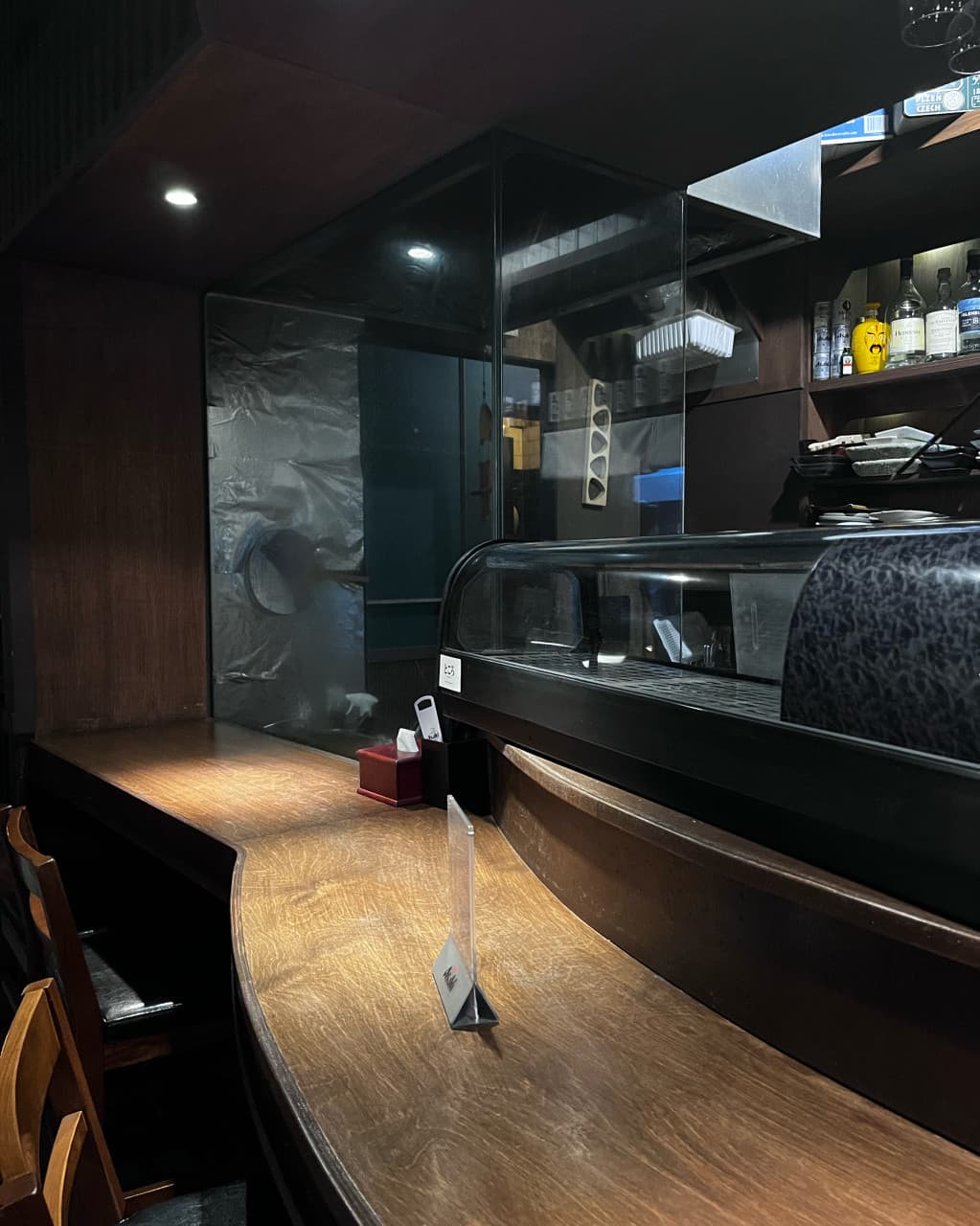 부산광역시 중구 도코로 남포동본점 이자카야의 조명 아래 놓인 곡선형 나무 다찌석. 1인 혼술이 가능한 카운터 좌석과 유리 진열장이 배치된 내부 공간.