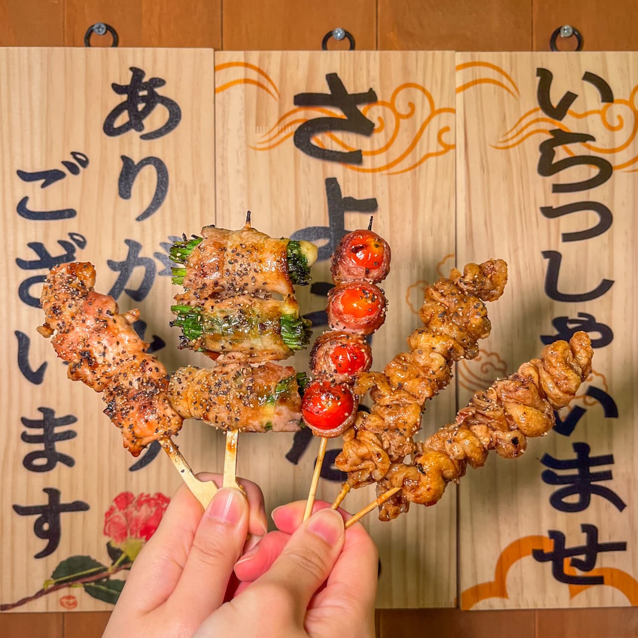 부산광역시 중구 이자카야별하 목판 앞에서 든 닭껍질과 베이컨 토마토 꼬치. 1인 혼술 이자카야 조명 아래 노릇하게 구워진 꼬치 5종의 질감과 다찌석 분위기.