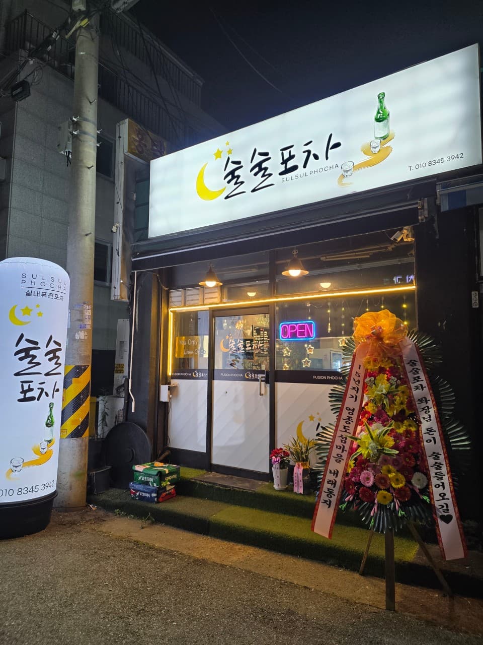 인천광역시 서구 술술포차 인천서구청 포장마차 - 노란 조명과 밝은 달 간판 아래 혼술 다찌석이 마련된 매장 입구와 축하 화환이 놓인 전경