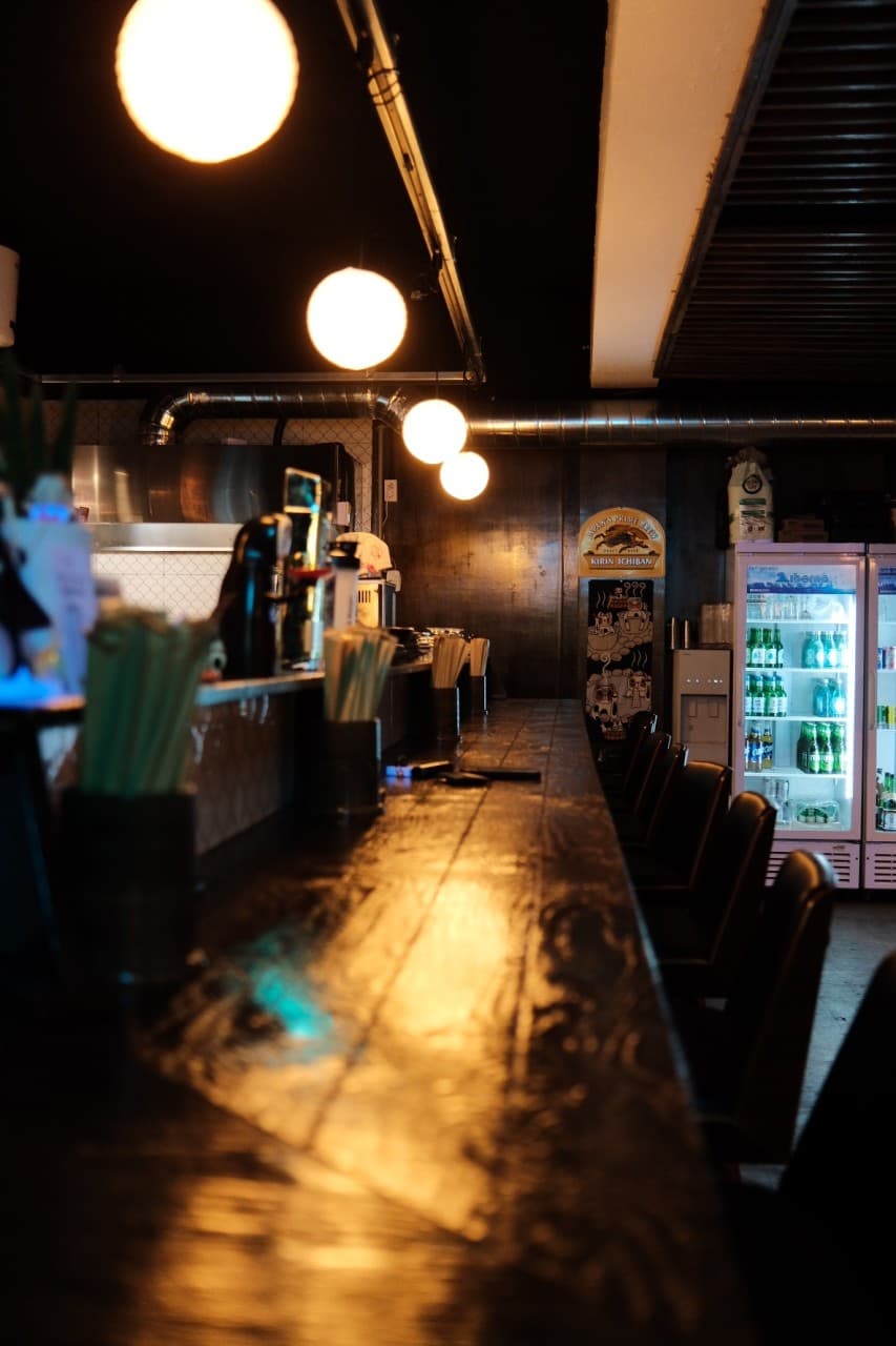 경상남도 창원시 도토나치 창원 이자카야의 원형 전구 조명 아래 놓인 나무 다찌석. 1인 좌석과 식기류가 준비된 혼술 전용 공간