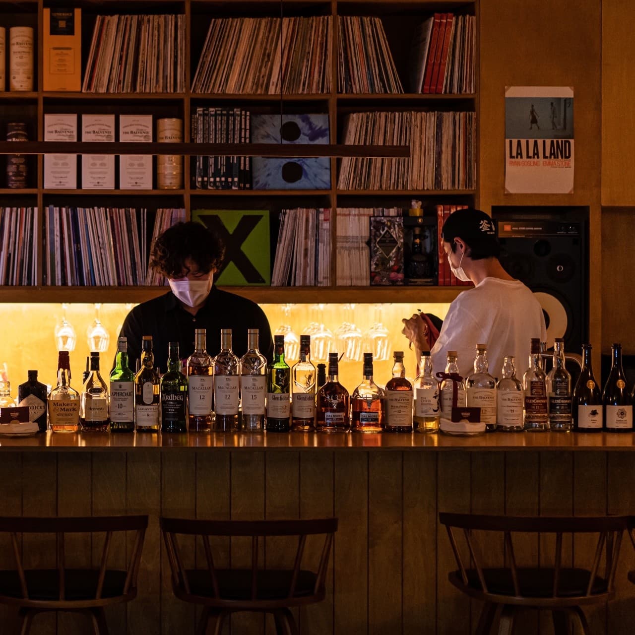 경상남도 진주시 요리주점 굿데이구디스 진주가좌본점 - 노란 조명과 LP 선반이 있는 다찌석에 위스키 병들이 진열된 1인 혼술 공간