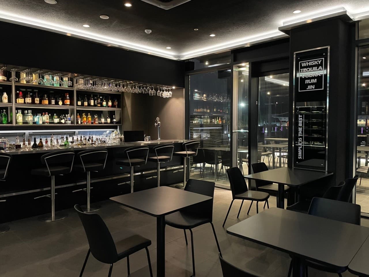 경상남도 진주시 마가리타 진주 바(Bar)의 간접 조명이 비치는 블랙 톤 다찌석과 1인용 바 체어. 벽면 선반에 진열된 위스키 보틀과 유리잔이 배치된 혼술 공간.