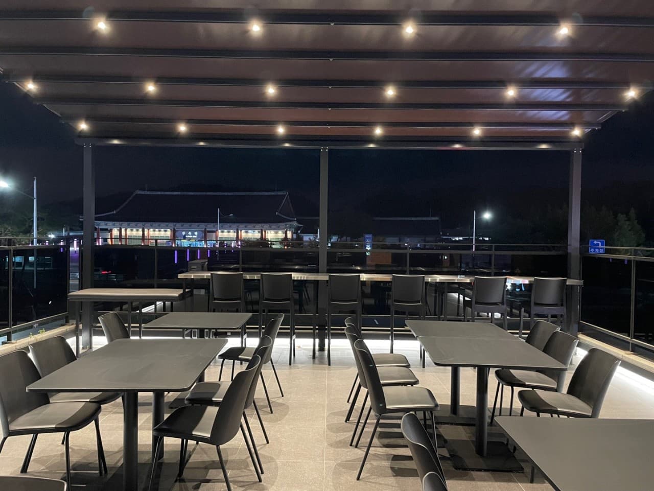 경상남도 진주시 마가리타 진주 바(Bar) 야외 테라스. 천장 조명 아래 다찌석과 테이블이 배치된 공간으로 진주역 야경을 바라보며 혼술 가능한 1인 좌석이 보임.