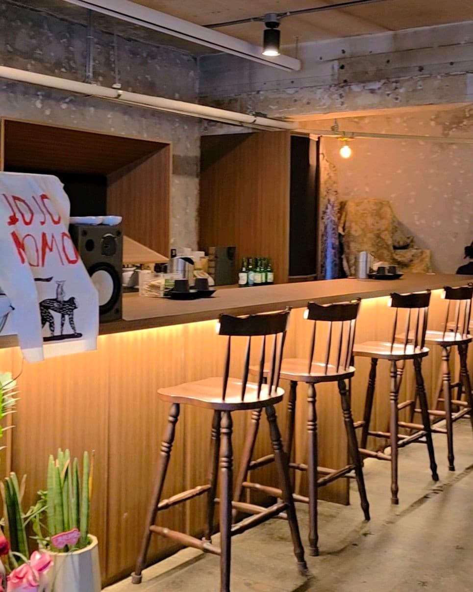 서울특별시 송파구 요리주점 조조모모. 하단 조명이 비치는 긴 나무 다찌석과 1인용 목재 의자가 배치된 혼술 좌석. 노출 콘크리트 벽면과 카운터 위 스피커가 있는 실내 구성.