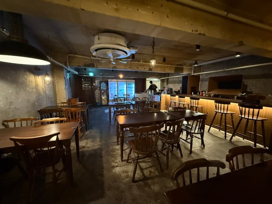 서울특별시 송파구 요리주점 조조모모 내부. 노란 전구 조명 아래 목재 테이블과 바 형태의 1인 다찌석이 있다. 콘크리트 질감의 벽면과 목재 가구가 배치된 혼술 공간을 보여준다.