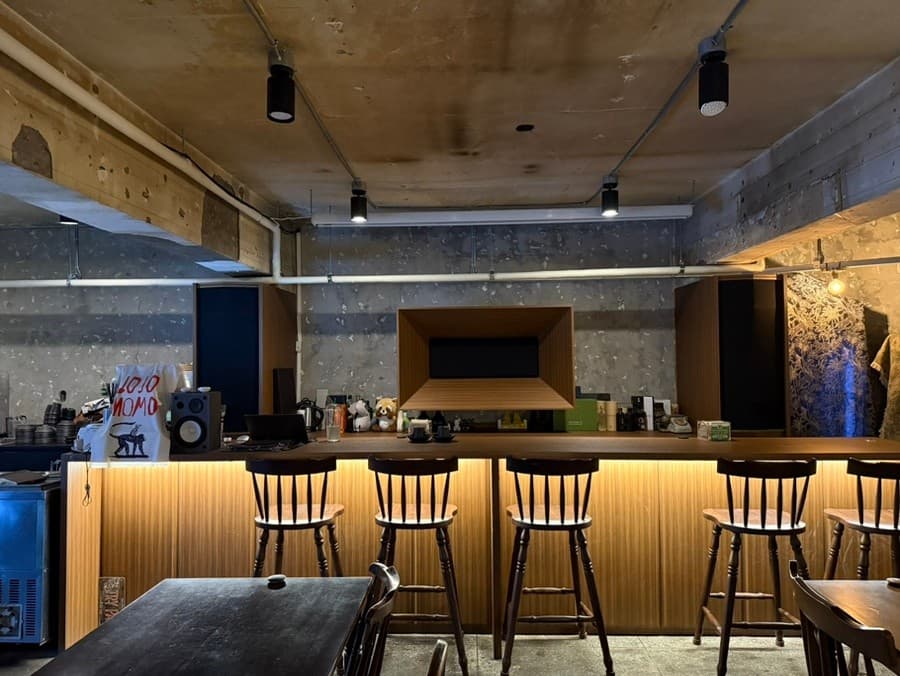 서울특별시 송파구 혼술 요리주점 조조모모 황색 간접 조명 아래 다찌석과 목재 의자가 놓인 1인 공간. 콘크리트 질감의 벽면과 바 테이블이 배치된 실내 구성.