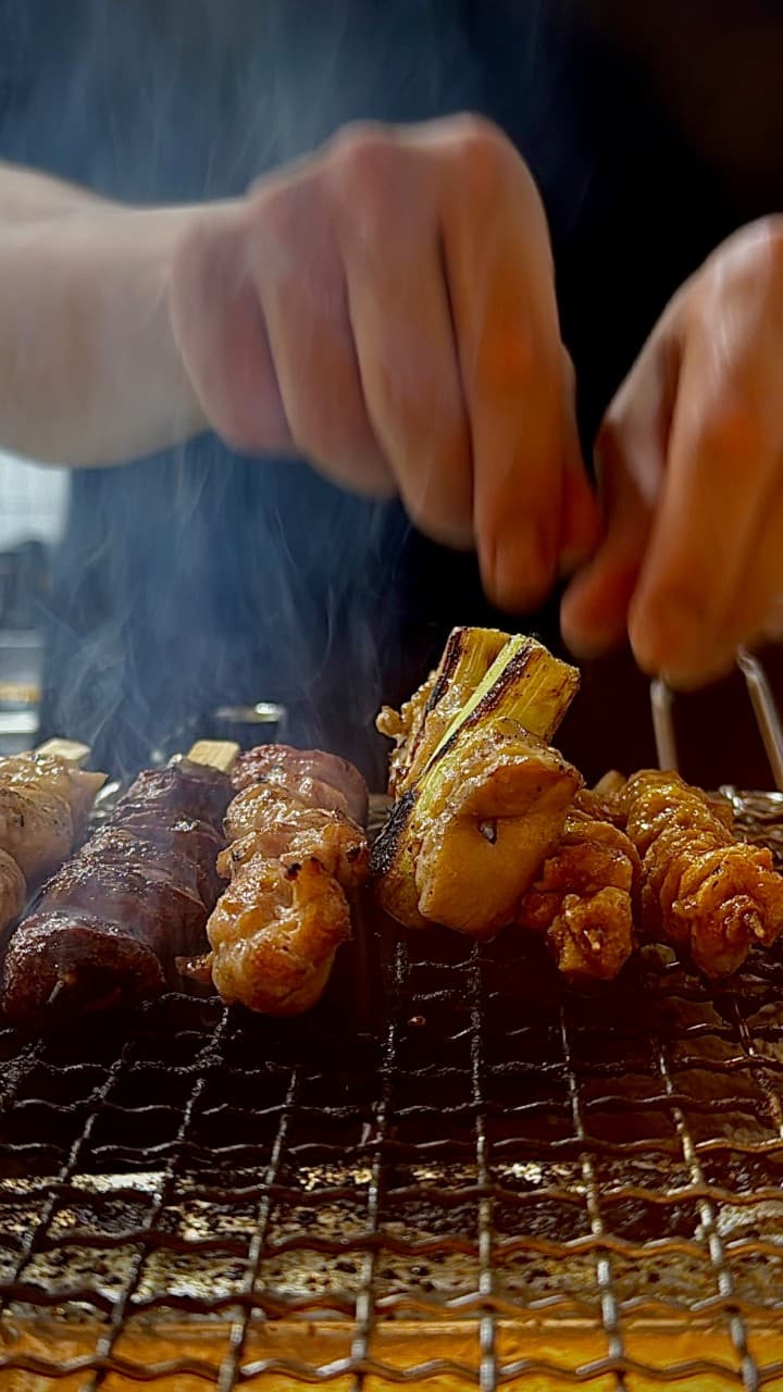 경상남도 진주시 이자카야 쿄오진 진주 다찌석에서 숯불 위 연기가 피어오르는 닭꼬치와 대파 구이의 질감을 보여주는 1인 혼술 상황
