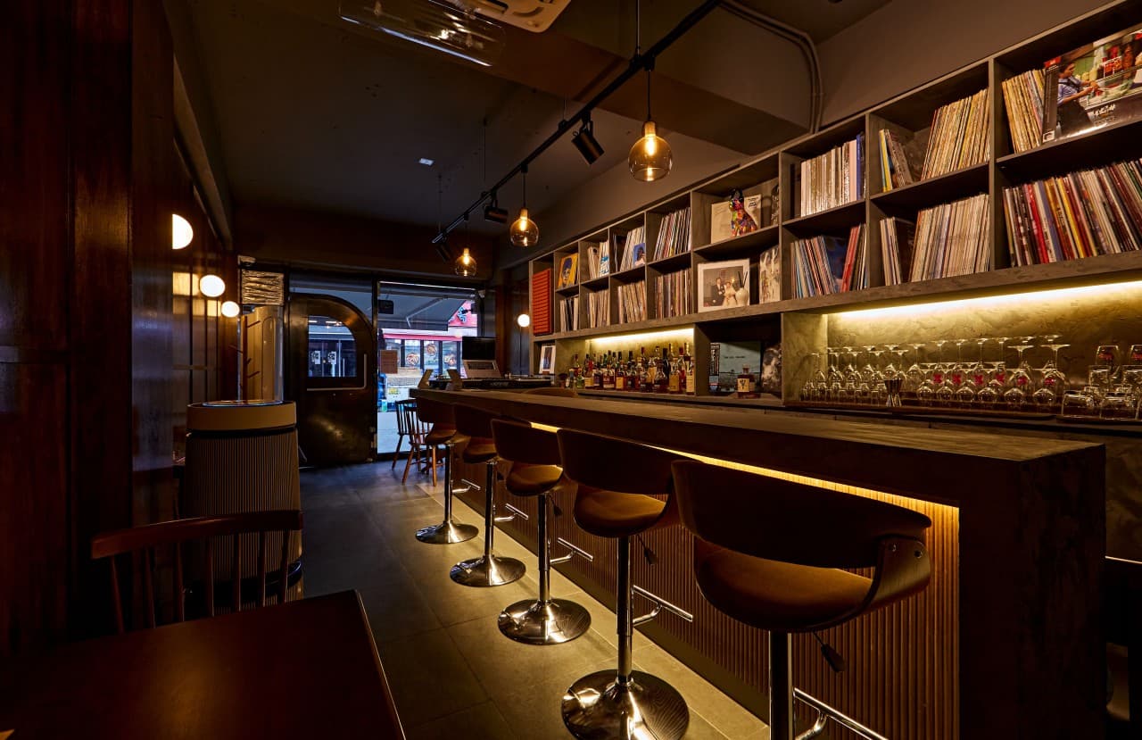 서울특별시 송파구 낭만LP바 잠실방이점 바(Bar)의 나무 소재 다찌석과 LP 레코드 선반. 낮은 조도의 조명 아래 1인석 의자가 배치되어 혼술을 즐기는 상황.