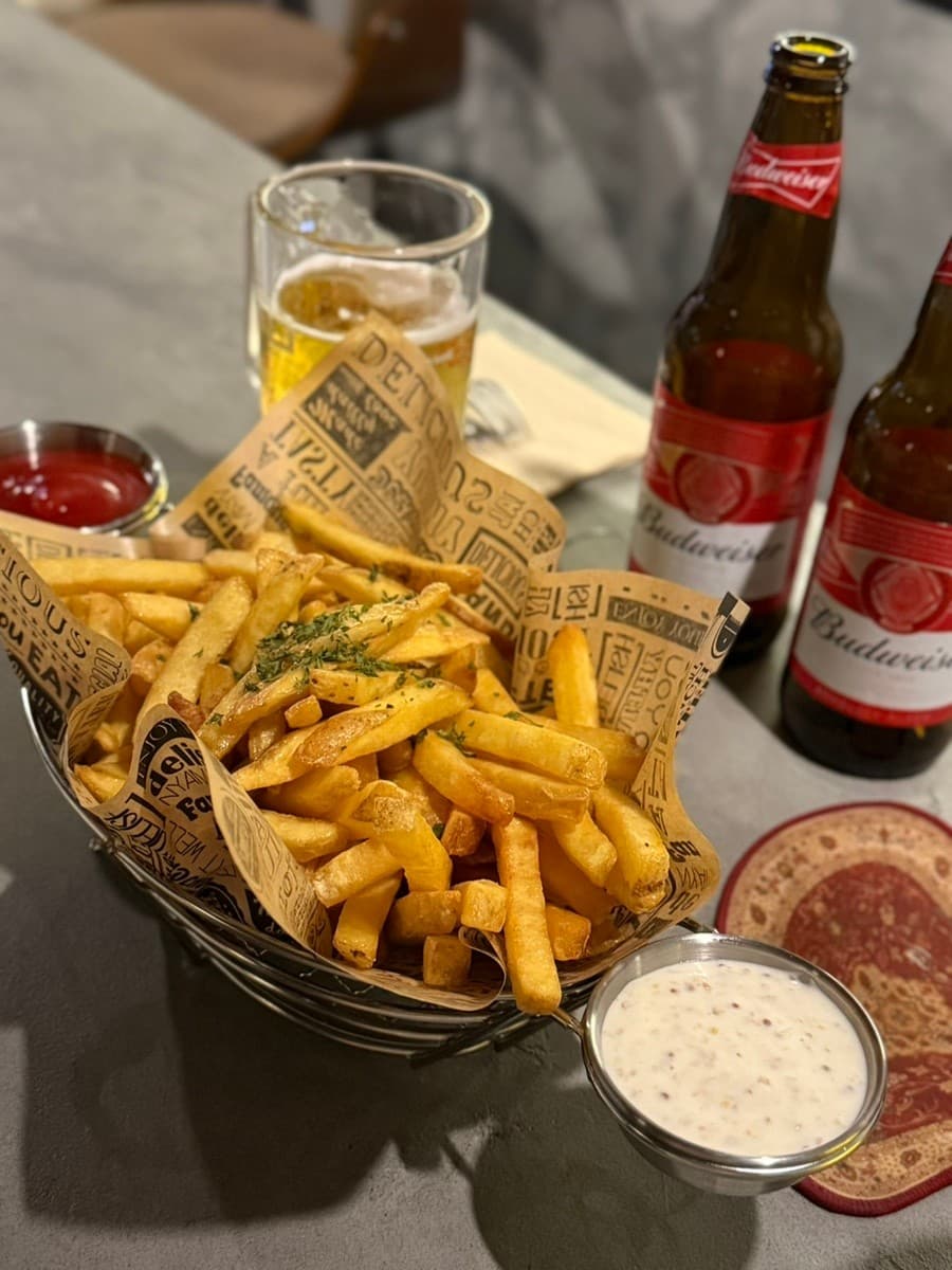 서울특별시 송파구 낭만LP바 잠실방이점 바(Bar) 다찌석에 차려진 혼술 차림. 바삭한 감자튀김과 버드와이저 병맥주가 놓인 1인석 테이블을 낮은 조명이 비춤.