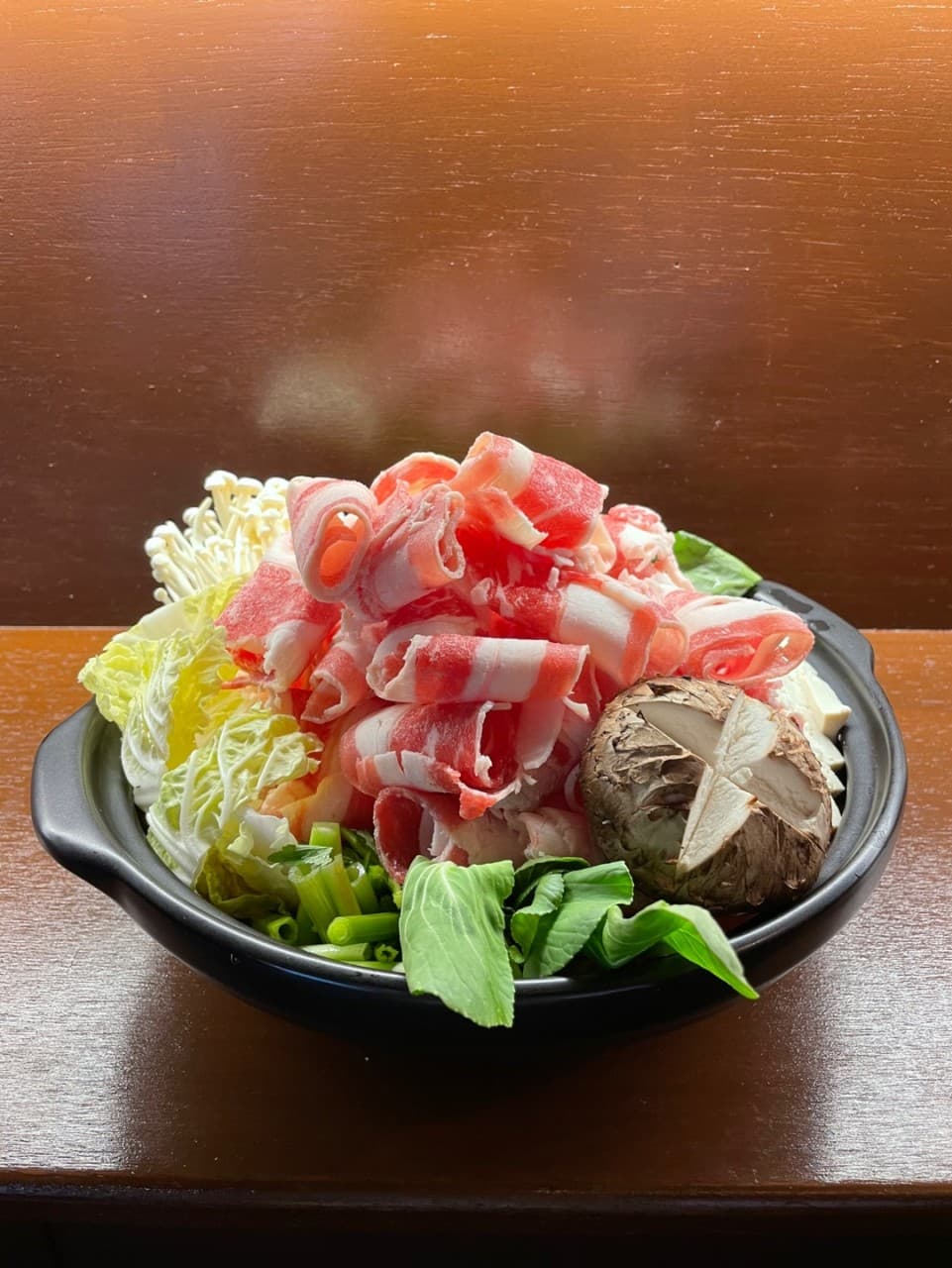 경상남도 진주시 요리주점 오코스 진주칠암본점 진주 다찌석에서 즐기는 1인 전골. 선홍빛 소고기와 표고버섯이 담긴 냄비가 나무 테이블 위 조명을 받는 상황.