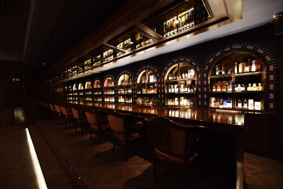 서울특별시 송파구 바 다빈치 잠실 바(Bar)의 어두운 조명 아래 긴 다찌석과 위스키가 진열된 아치형 선반들. 1인 혼술에 적합한 카운터 좌석과 어두운 실내 환경을 보여줌.