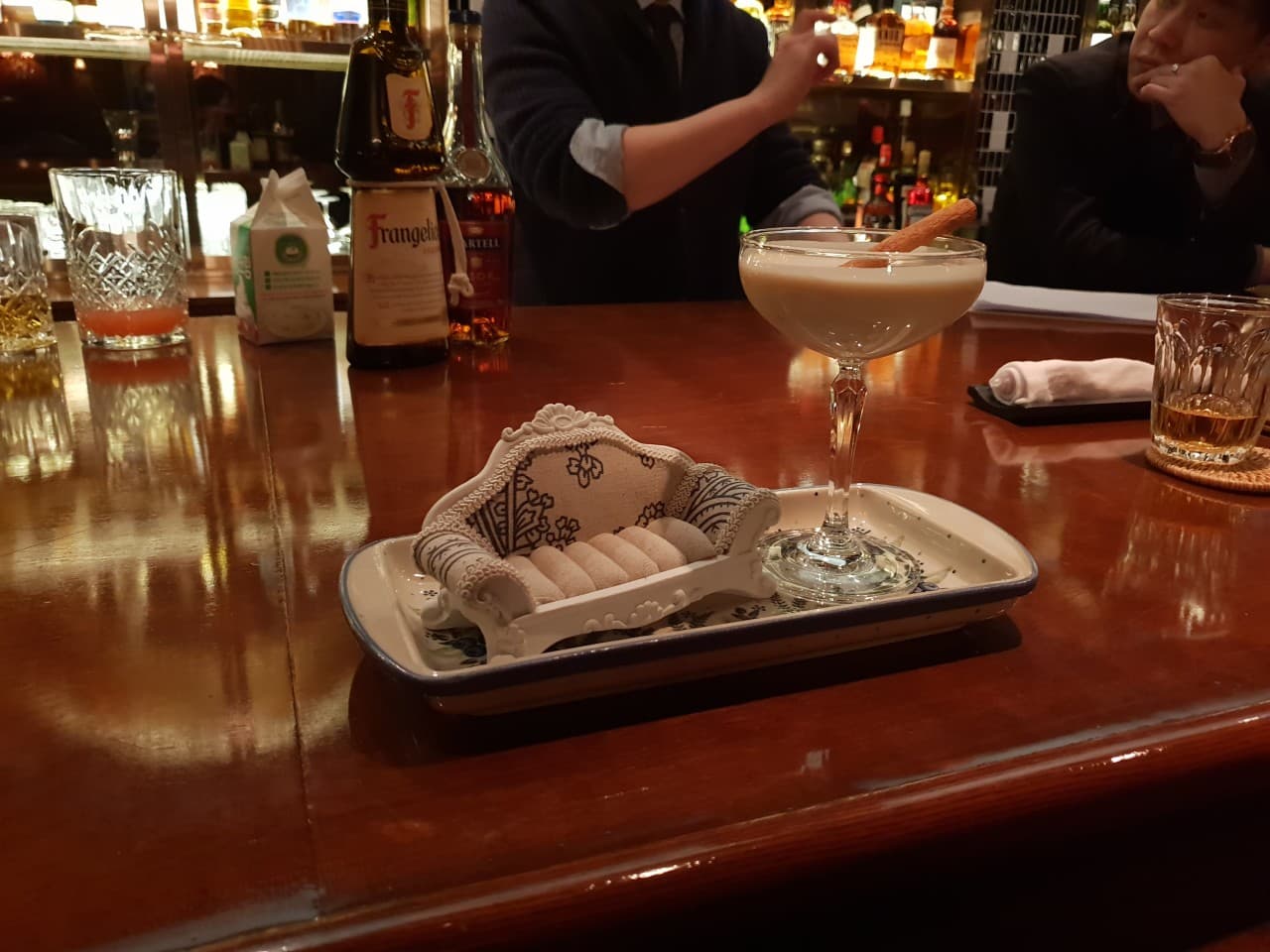 서울특별시 송파구 바 다빈치 잠실 다찌석 위 크림 칵테일과 시나몬 스틱. 조명 비치는 술병 진열장 앞 1인 카운터 바(Bar)에서 혼술을 즐기는 상황.