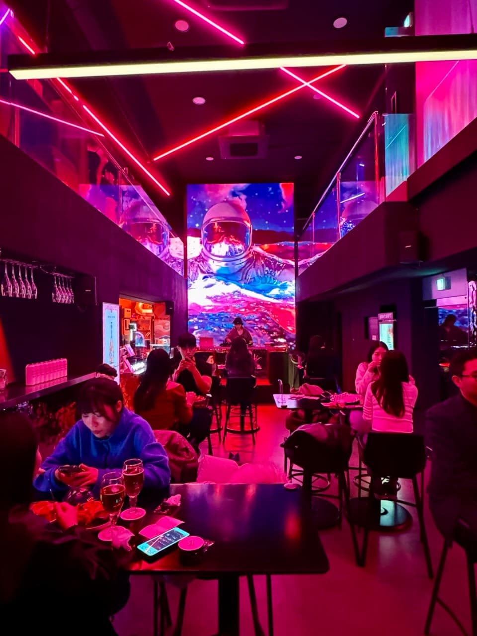 서울특별시 송파구 나쉬펍 잠실방이점 맥주 호프 - 분홍색 네온 조명과 대형 우주인 스크린 아래 1인 다찌석에서 맥주를 즐기는 혼술 상황