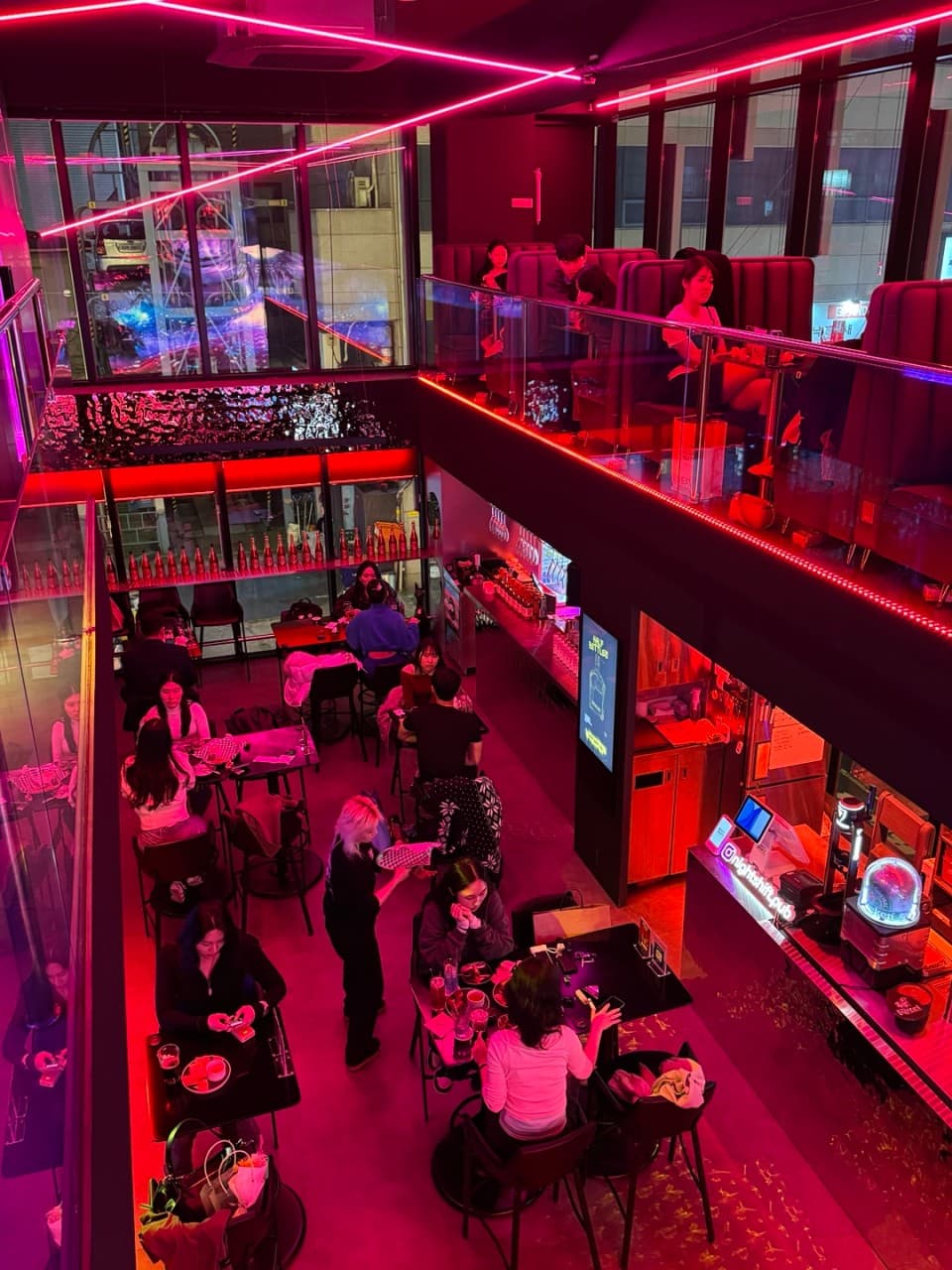 서울특별시 송파구 나쉬펍 잠실방이점의 붉은 네온 조명이 비치는 복층 다찌석과 테이블. 맥주 호프를 즐기는 사람들과 1인 혼술객을 위한 바 좌석이 마련된 내부 전경.