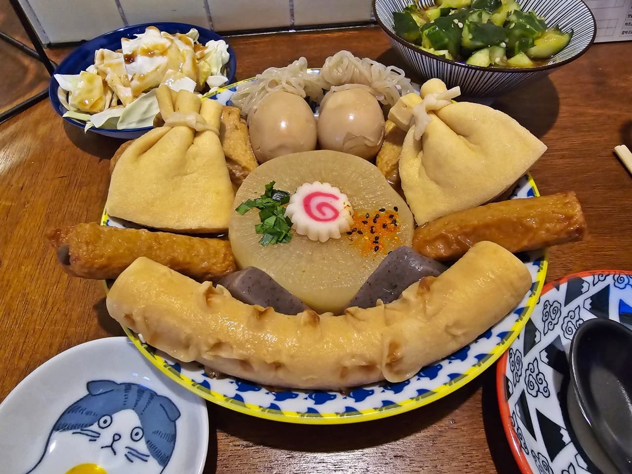 서울특별시 송파구 이자카야 오뎅바모츠뎅 잠실 다찌석. 조명 아래 무와 유부주머니가 담긴 1인 오뎅 모듬과 밑반찬이 차려진 혼술 테이블.