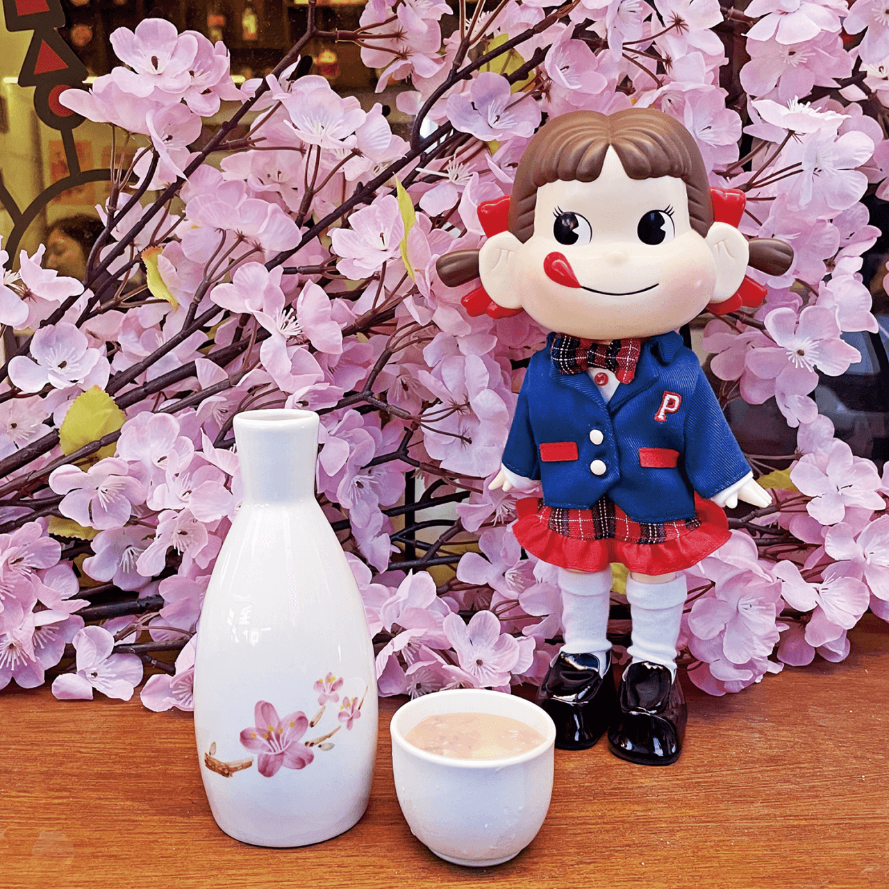 서울특별시 송파구 오뎅바모츠뎅 잠실 이자카야 1인 다찌석. 분홍색 벚꽃 배경과 페코짱 인형 앞 도자기 술병 및 잔이 놓인 혼술 현장.