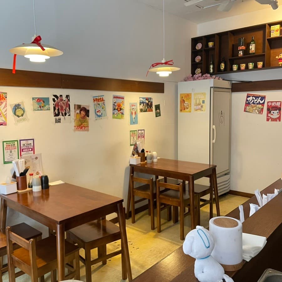 서울특별시 송파구 오뎅바모츠뎅 잠실 이자카야의 펜던트 조명과 1인 다찌석. 나무 테이블과 벽면 포스터가 배치된 실내 공간에서 혼술을 즐기는 상황을 보여줌.