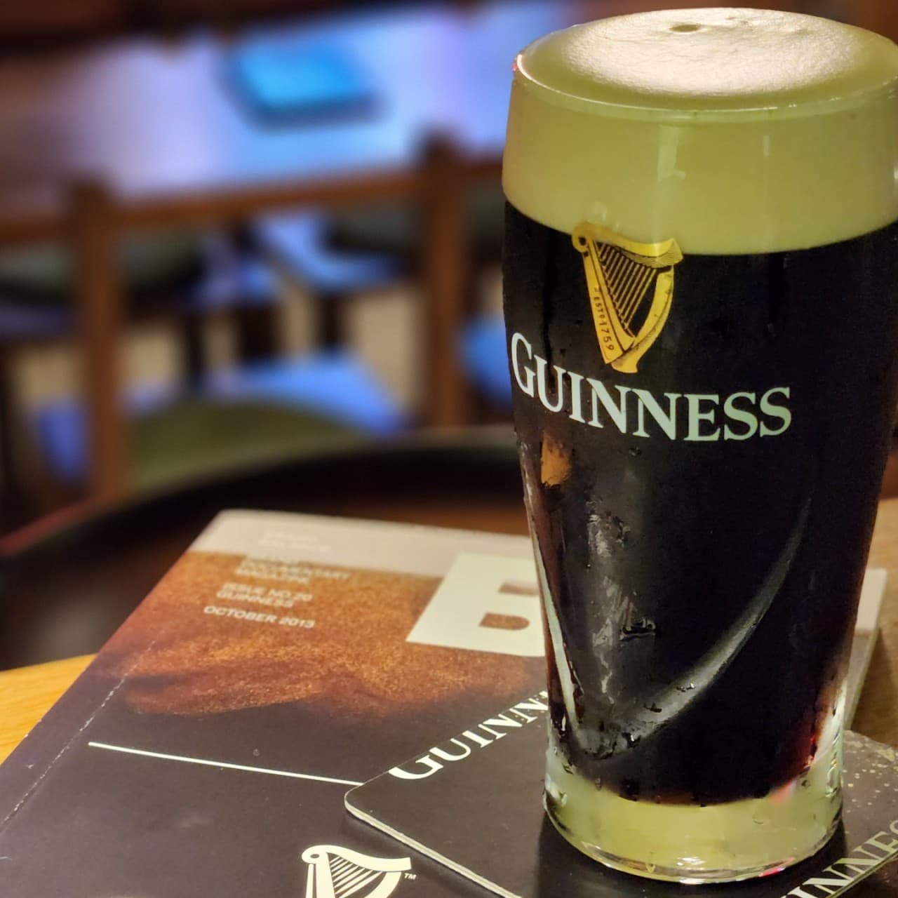 경상남도 진주시 진주탭룸 진주 혼술 - 하얀 거품이 올라온 기네스 흑맥주와 잡지가 놓인 다찌석. 기타 주류를 즐기는 1인석 테이블과 조명이 비치는 상황.