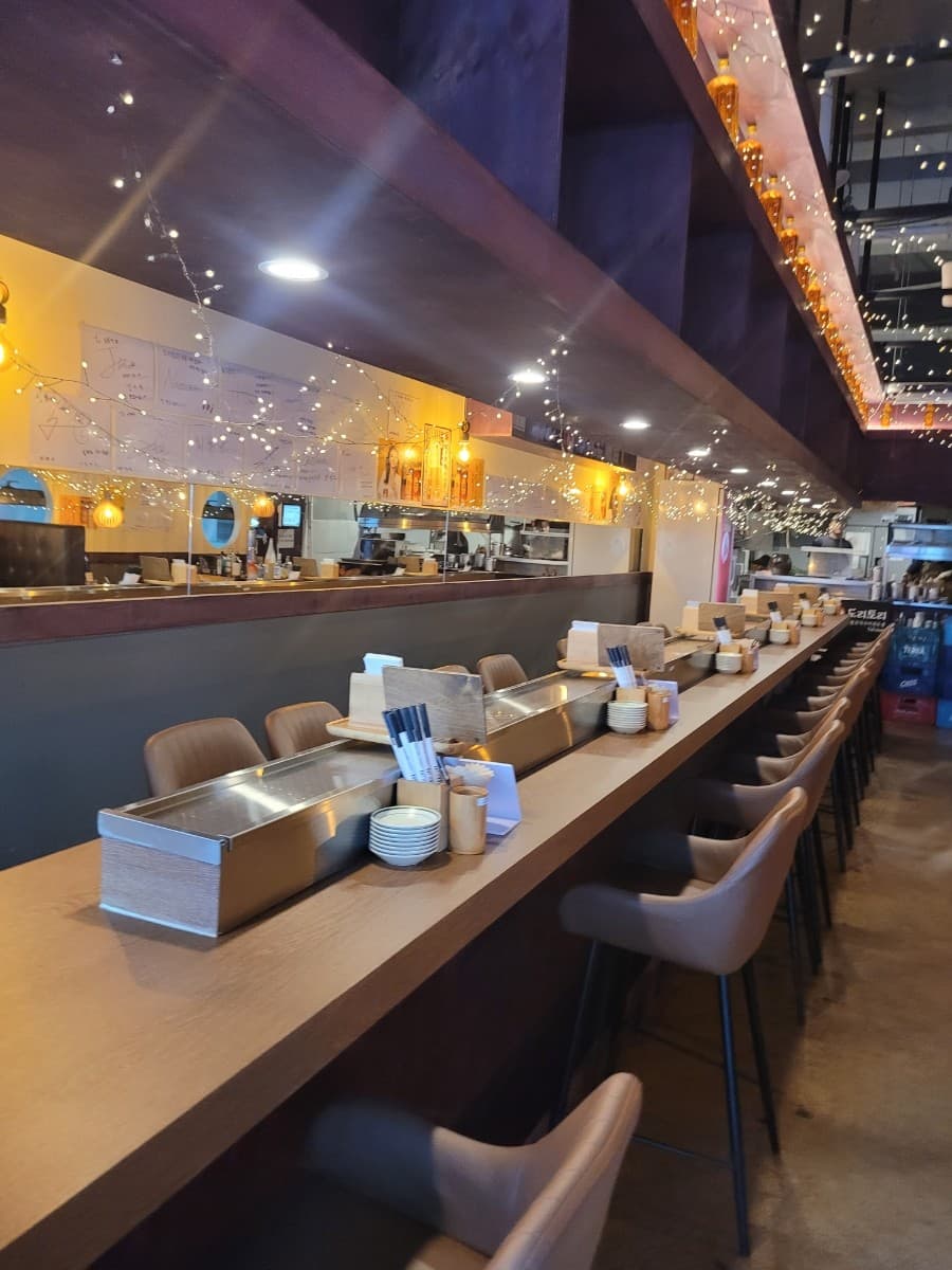 대전광역시 유성구 요리주점 도리토리 대전봉명점의 전구 조명이 비추는 긴 다찌석. 혼술용 1인 좌석과 원목 카운터 위 일렬로 정돈된 식기류.