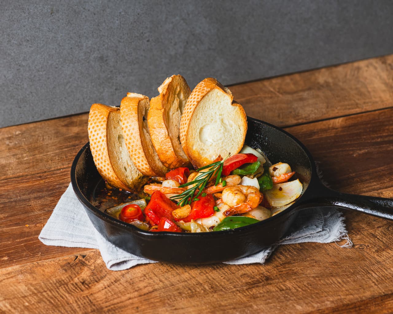 서울특별시 강남구 맥주 호프 전문점 아이러브펍 강남본점 1인 혼술. 나무 테이블 위 무쇠 팬에 담긴 새우 감바스와 바게트가 조명 아래 놓여 있는 상황.