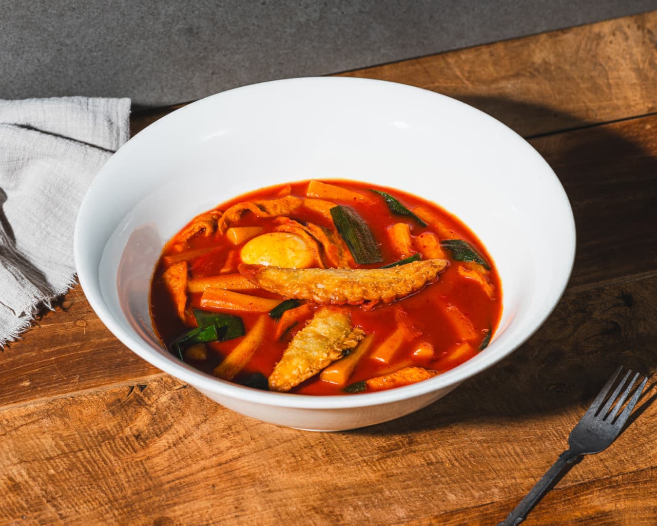 서울특별시 강남구 아이러브펍 강남본점 맥주 호프 매장 나무 테이블 위 튀김만두가 올라간 떡볶이와 포크. 조명 아래 붉은 양념 질감이 선명한 1인 혼술 안주 차림.