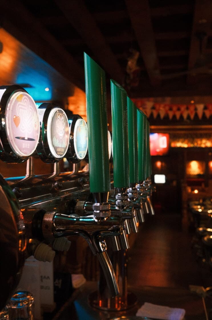 서울특별시 강남구 맥주 호프 아이러브펍 강남본점. 주황색 조명 아래 다찌석 카운터에 정렬된 초록색 생맥주 탭이 보이는 1인 혼술 공간.