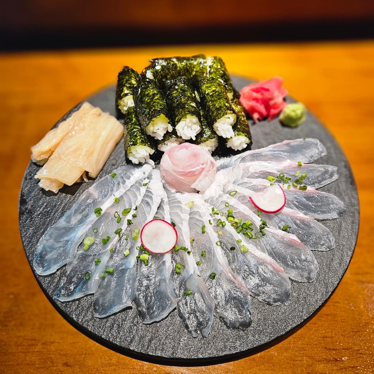 서울특별시 강남구 이자카야 고코 강남신논현점 다찌석 조명 아래 놓인 1인 사시미와 김초밥. 투명한 생선회 질감과 나무 테이블이 보이는 혼술 상황의 구성.