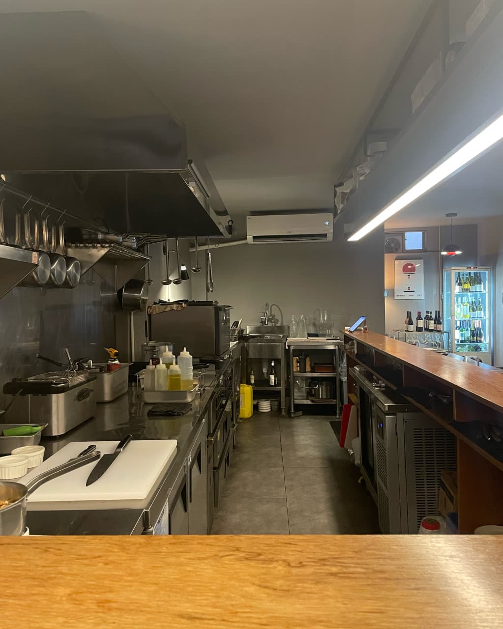 대구광역시 중구 와인바 러프 대구 동성로의 오픈형 주방과 다찌석. 직선 조명 아래 정돈된 스테인리스 조리 기구와 와인 냉장고가 위치한 1인 혼술 전용 카운터 좌석 구조.