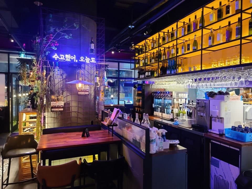 서울특별시 강남구 오늘와인한잔 강남역 - 노란 조명 아래 진열된 와인 병들과 1인 다찌석에서 보라색 네온사인을 배경으로 와인을 즐기는 혼술 상황