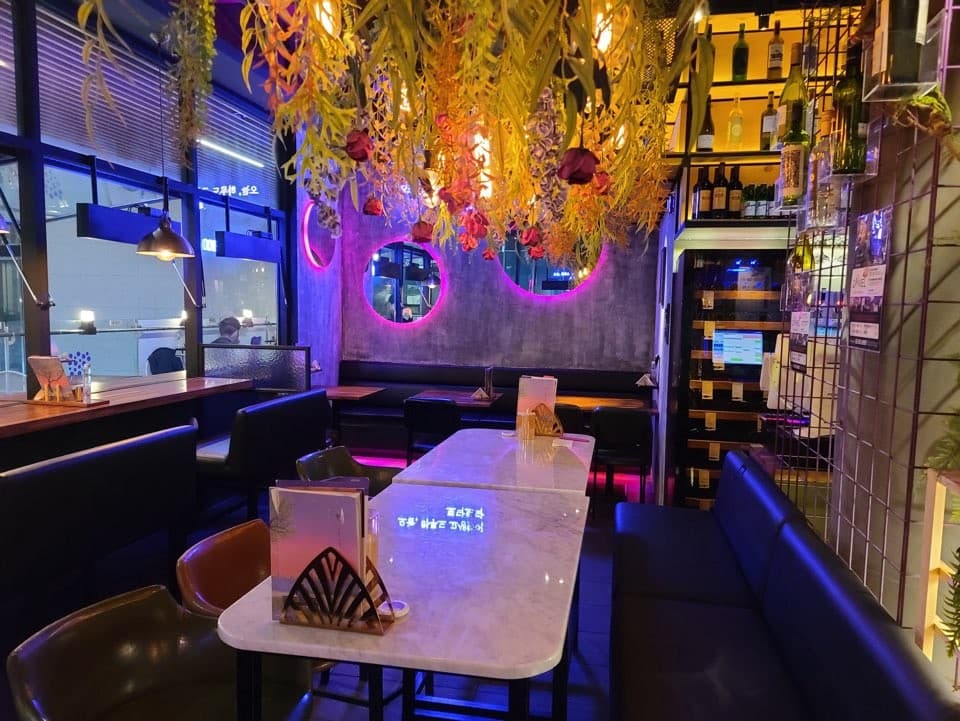 서울특별시 강남구 오늘와인한잔 강남역 와인 매장 보랏빛 조명과 천장 식물 장식 아래 구성된 대리석 테이블 및 창가 1인 다찌석 혼술 공간