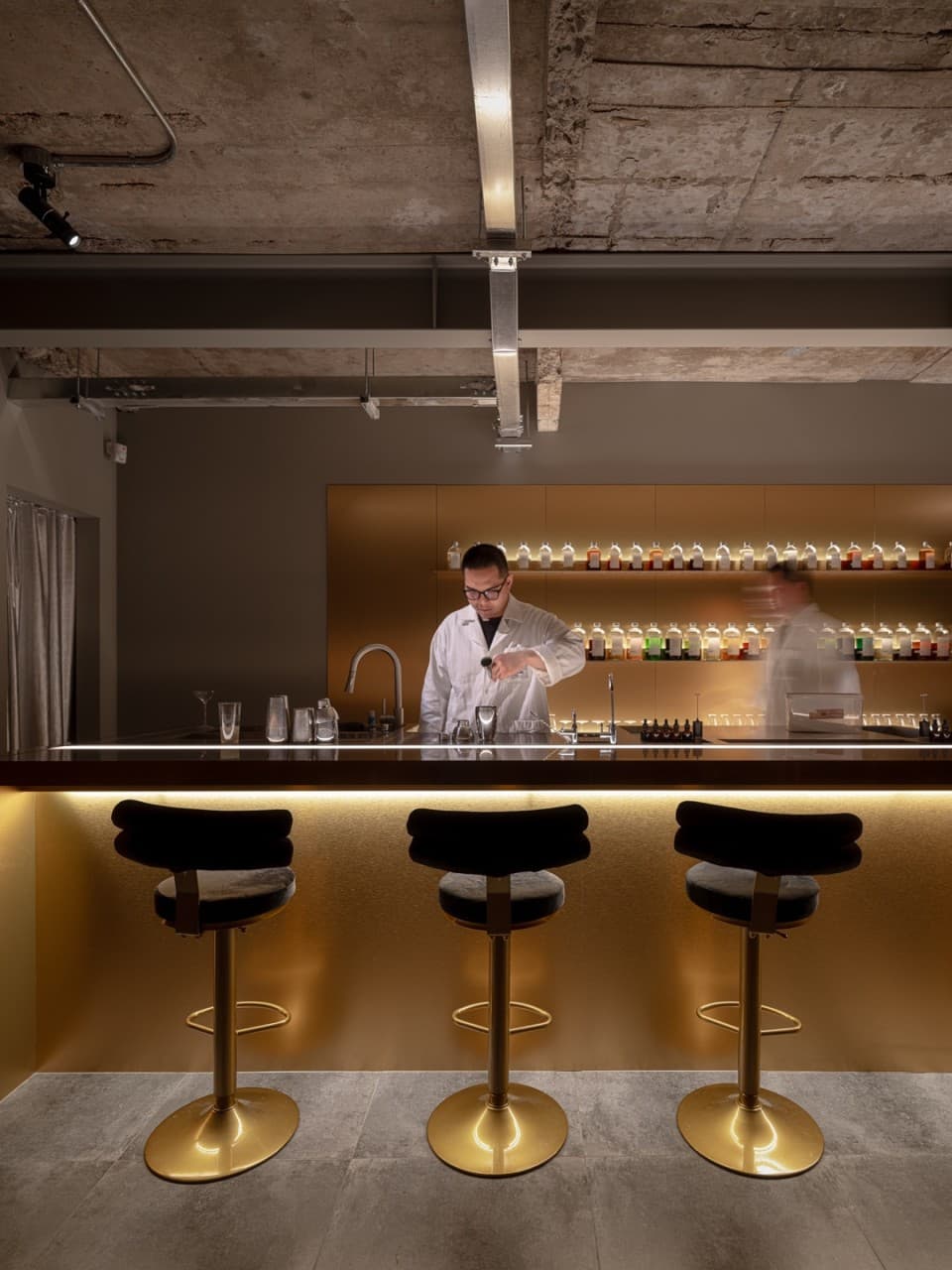 부산광역시 수영구 코듀로이 벨라즈 광안리 바(Bar) 혼술 1인 다찌석 - 황금빛 조명 아래 길게 뻗은 카운터 테이블과 칵테일을 조제하는 바텐더