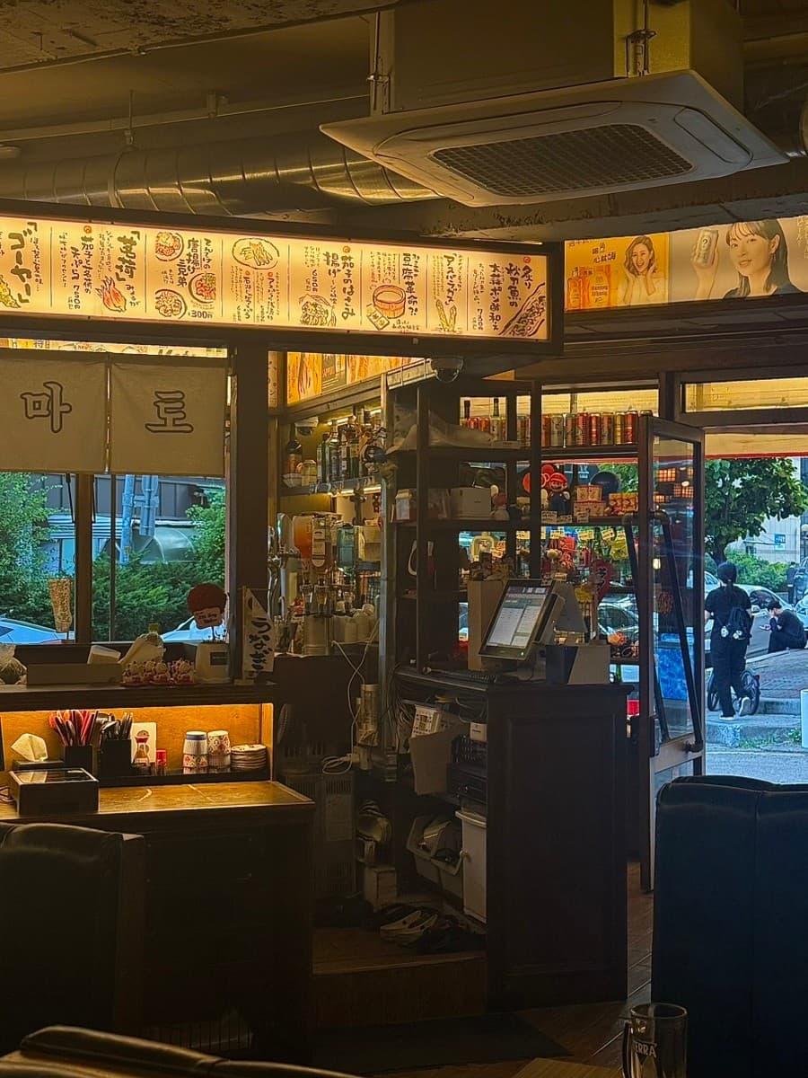 인천광역시 남동구 요리주점 하나마토 인천 구월동 - 노란 조명의 일본식 메뉴판 아래 1인 다찌석이 마련된 모습. 혼술 가능한 카운터 좌석과 식기류가 배치된 내부.