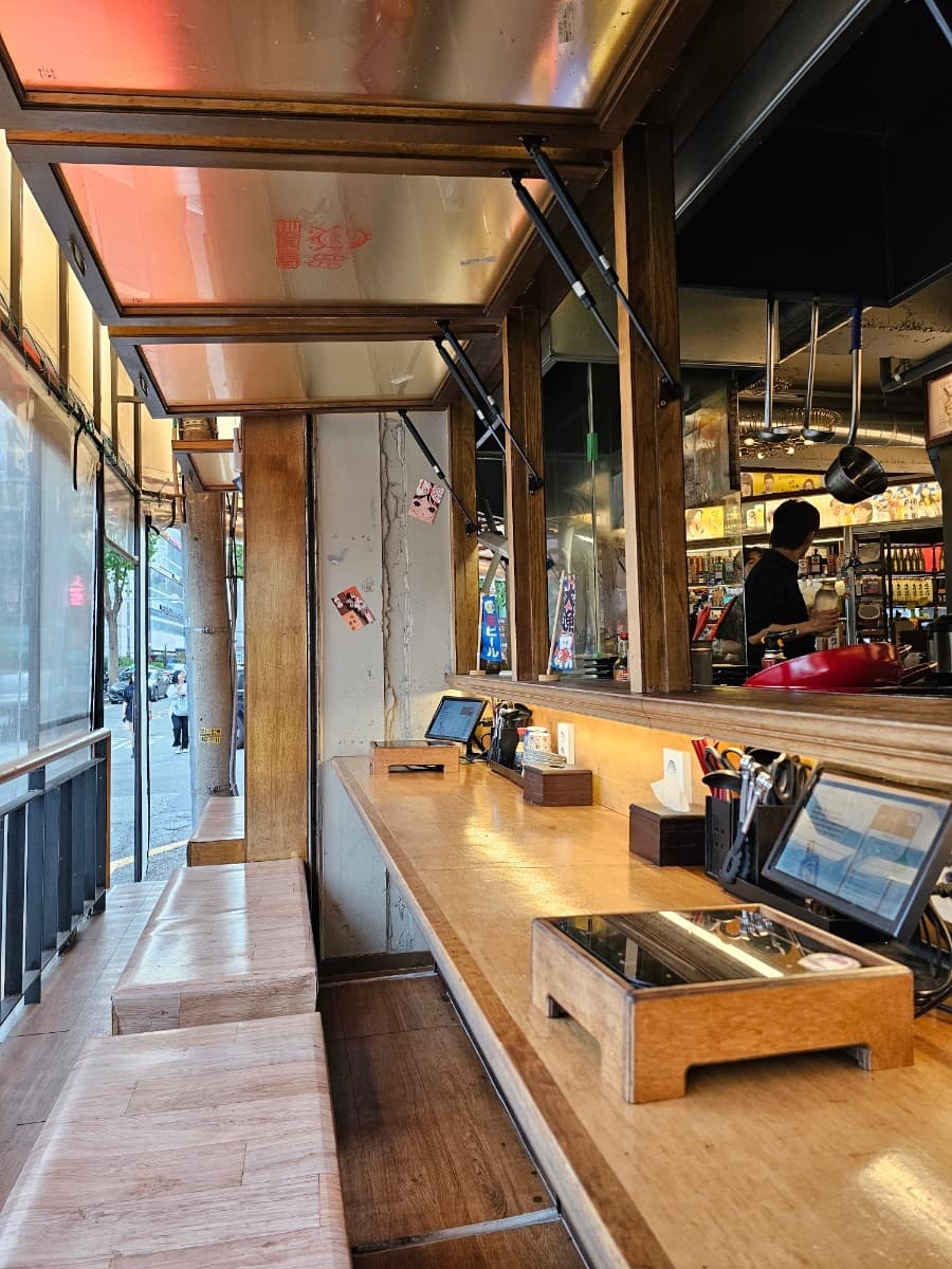 인천광역시 남동구 요리주점 하나마토 인천 구월동의 오렌지빛 조명 아래 길게 이어진 나무 다찌석과 1인 혼술용 태블릿이 배치된 좌석 모습.