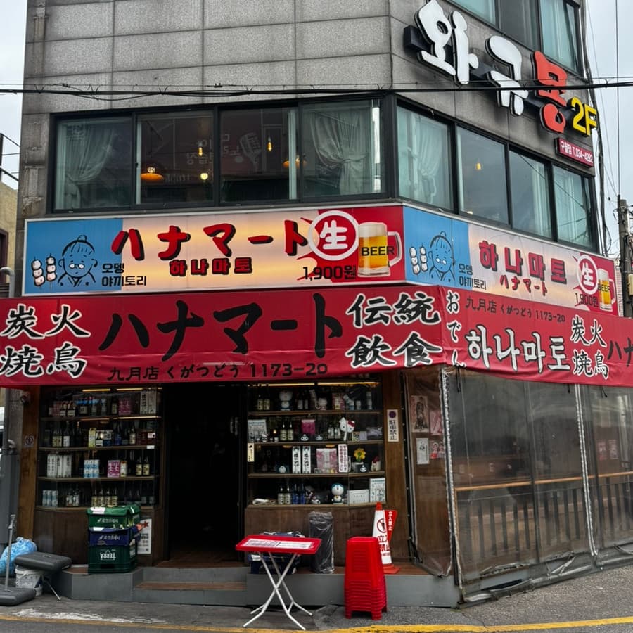 인천광역시 남동구 요리주점 하나마토 인천 구월동. 일본풍 붉은 천막과 사케 병이 진열된 다찌석에서 혼술 하는 상황. 야키토리와 생맥주 간판이 부착된 건물 1층 외경.