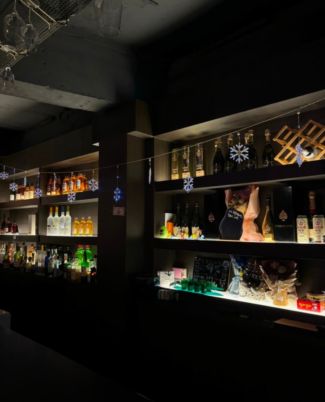 경기도 의정부시 크라운 칵테일바 - 선반 조명 아래 진열된 위스키 병들과 눈송이 장식물. 1인 다찌석이 배치된 어두운 실내에서 혼술하는 상황.
