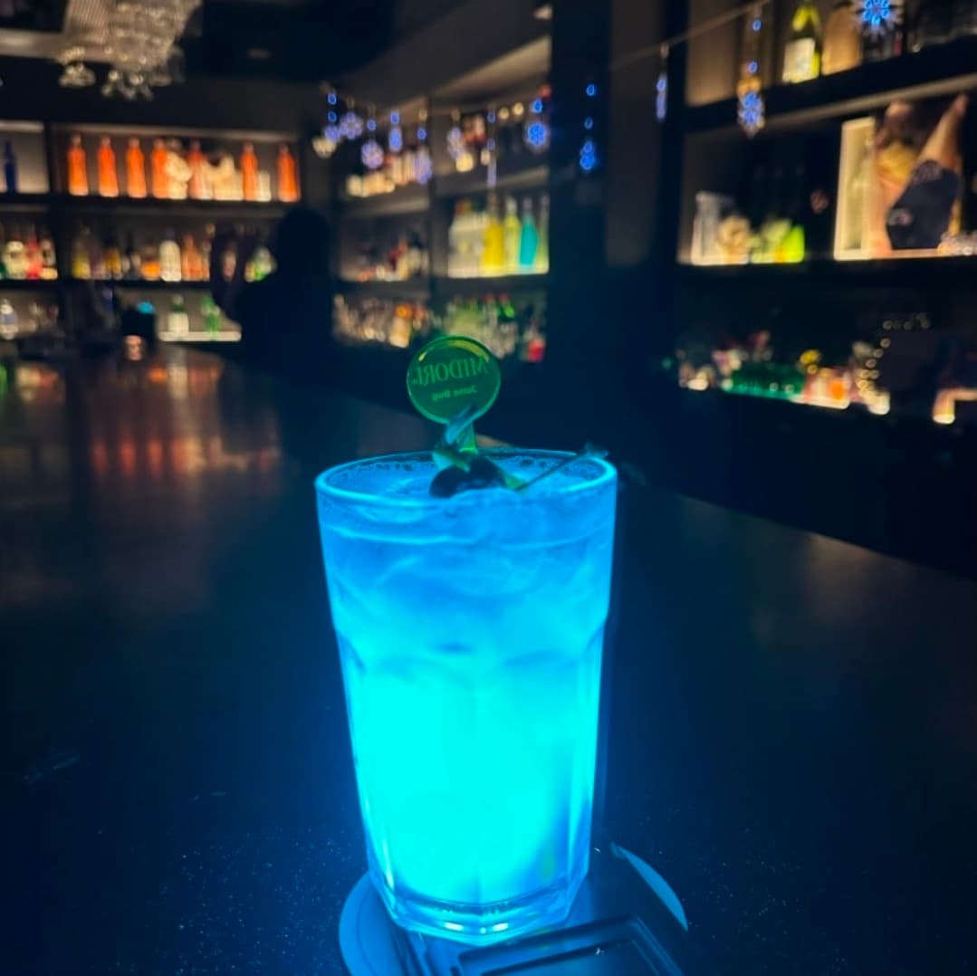 경기도 의정부시 칵테일바 크라운의 다찌석에 놓인 형광 푸른색 칵테일. 배경의 진열된 술병들과 어두운 조명 아래서 즐기는 1인 혼술 상황.
