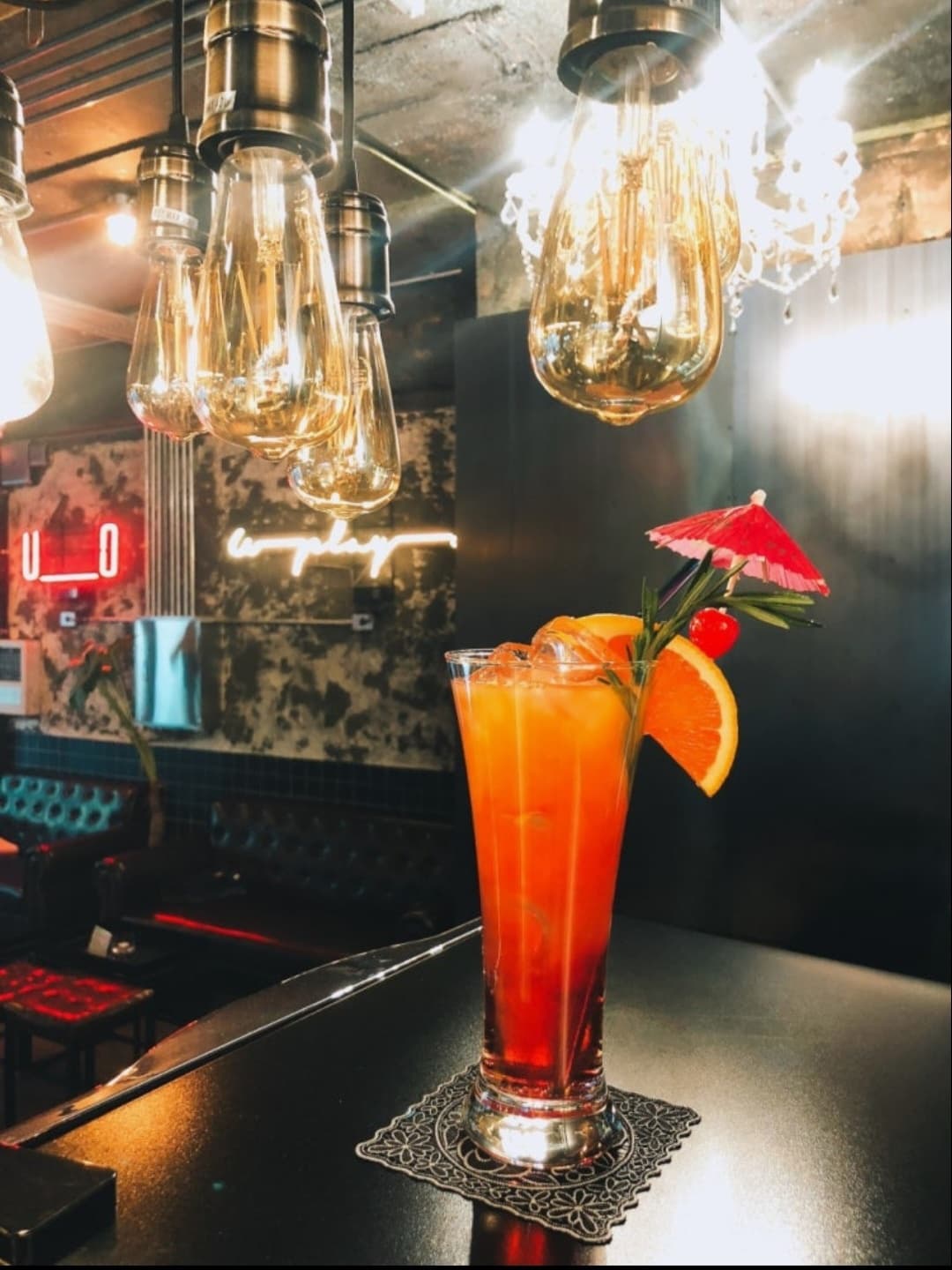 경기도 의정부시 유플레이온 바 다찌석 위 오렌지 슬라이스가 담긴 칵테일. 에디슨 전구 조명 아래 1인석에서 혼술을 즐기는 상황