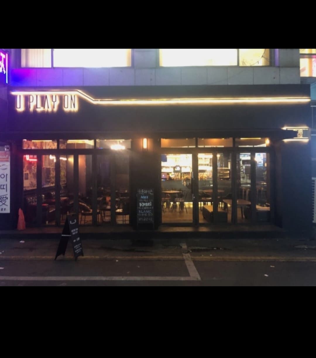 경기도 의정부시 유플레이온 바 외부 전경. 노란 선형 조명이 빛나는 검은색 벽면과 유리창 안쪽의 혼술 테이블, 입구에 배치된 메뉴판의 배치 상황.