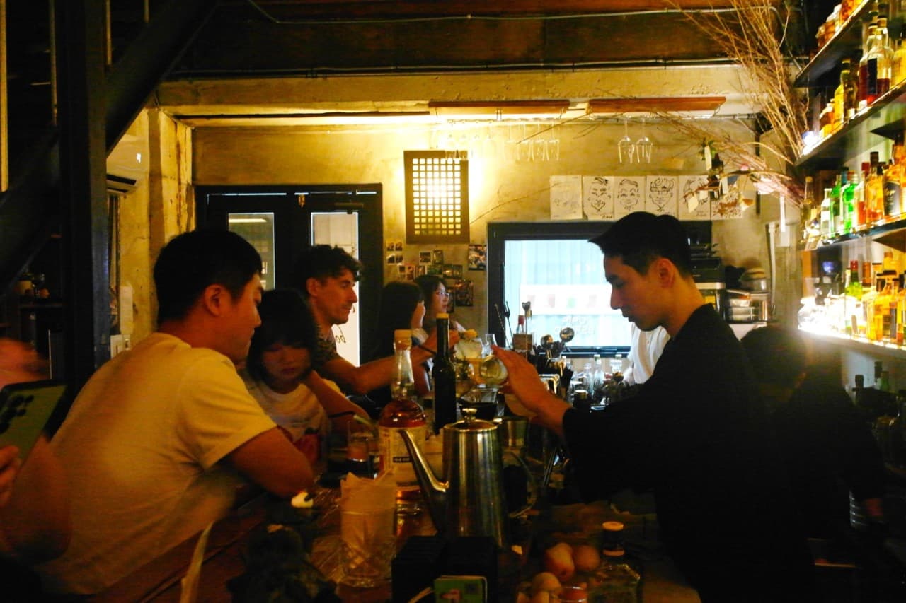 경상북도 경주시 BAR분 경주 바의 노란 조명 아래 긴 나무 다찌석과 술병 선반. 바텐더가 음료를 제조하며 1인 손님이 착석한 혼술 중심의 내부 상황.