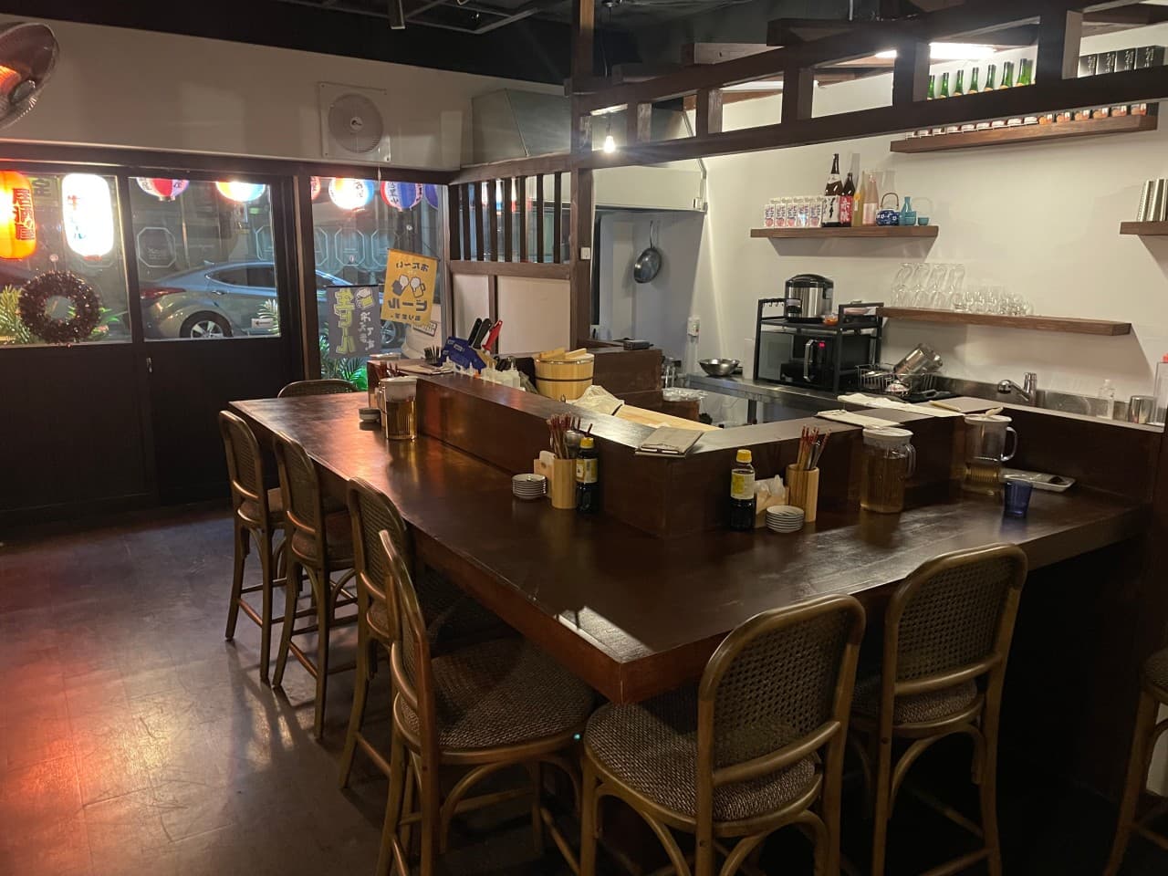 경상북도 경주시 다카라초 경주 이자카야의 목재 다찌석과 1인 의자. 주황색 조명 아래 술병이 진열된 선반과 주방이 보이는 혼술 중심의 매장 내부 전경.