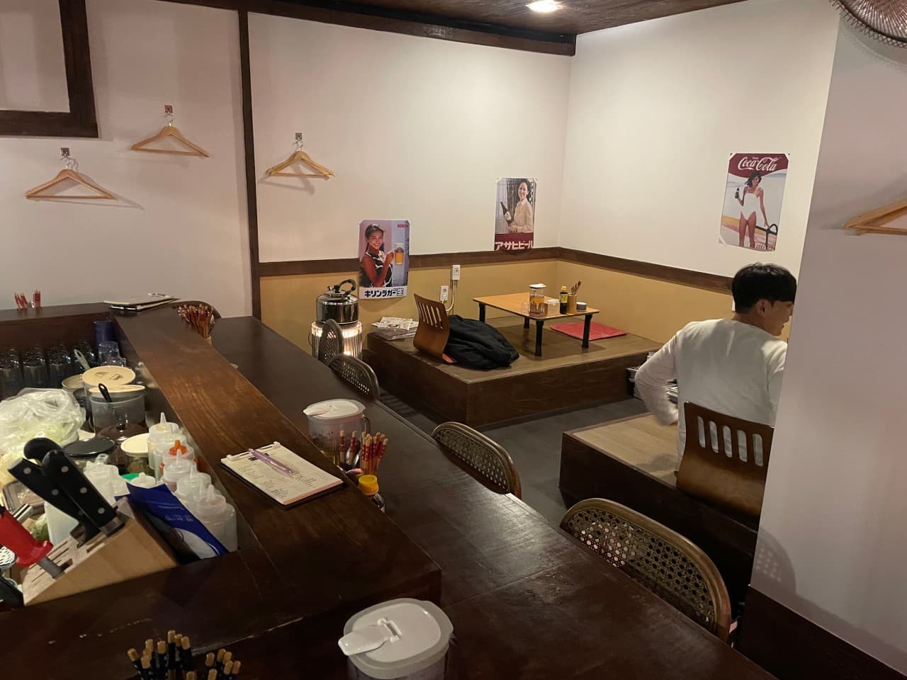 경상북도 경주시 다카라초 경주 이자카야 - 나무 소재 다찌석과 평상형 테이블이 있는 1인 혼술 공간. 벽면의 포스터와 옷걸이, 주방 도구들이 배치된 목조 인테리어 구성.