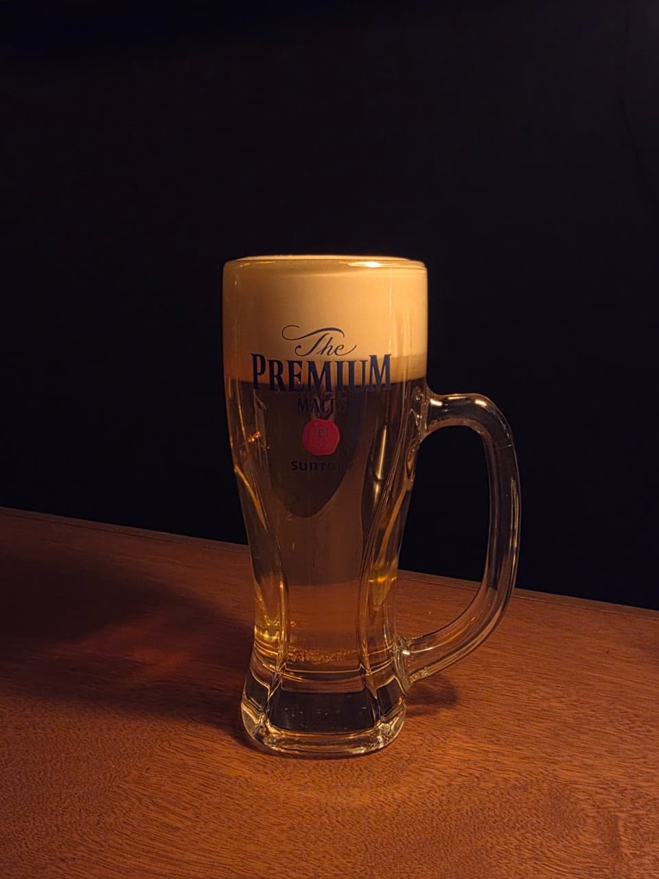 경상북도 경주시 혼술바 포 경주 바(Bar) 다찌석 원목 테이블 위 조명을 받은 산토리 생맥주의 하얀 거품과 탄산 질감. 1인 혼술 상황을 묘사.