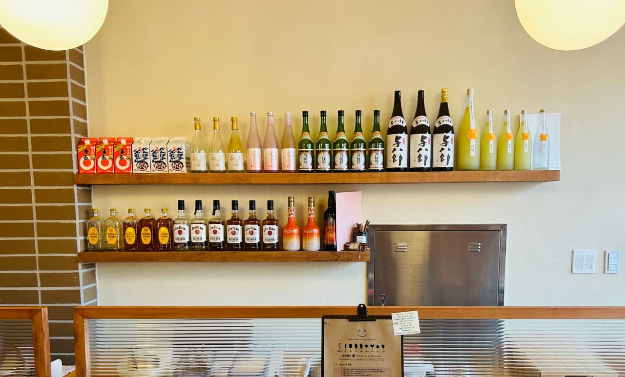 경상북도 경주시 텐고쿠 경주 매장 내부. 원형 조명 아래 다양한 주류 병이 진열된 2단 선반과 유리 칸막이가 설치된 1인 다찌석. 혼술을 위한 좌석이 마련된 기타 업종 식당 전경.