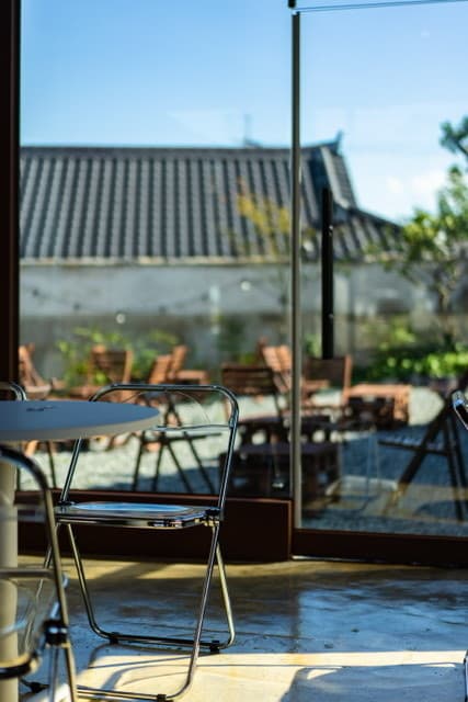 경상북도 경주시 황남주택 경주 맥주 호프 창가에 비치는 자연광. 크롬 의자와 테이블 너머로 기와지붕과 마당이 보이며 혼술 하기 적합한 1인석 상황을 보여줌.