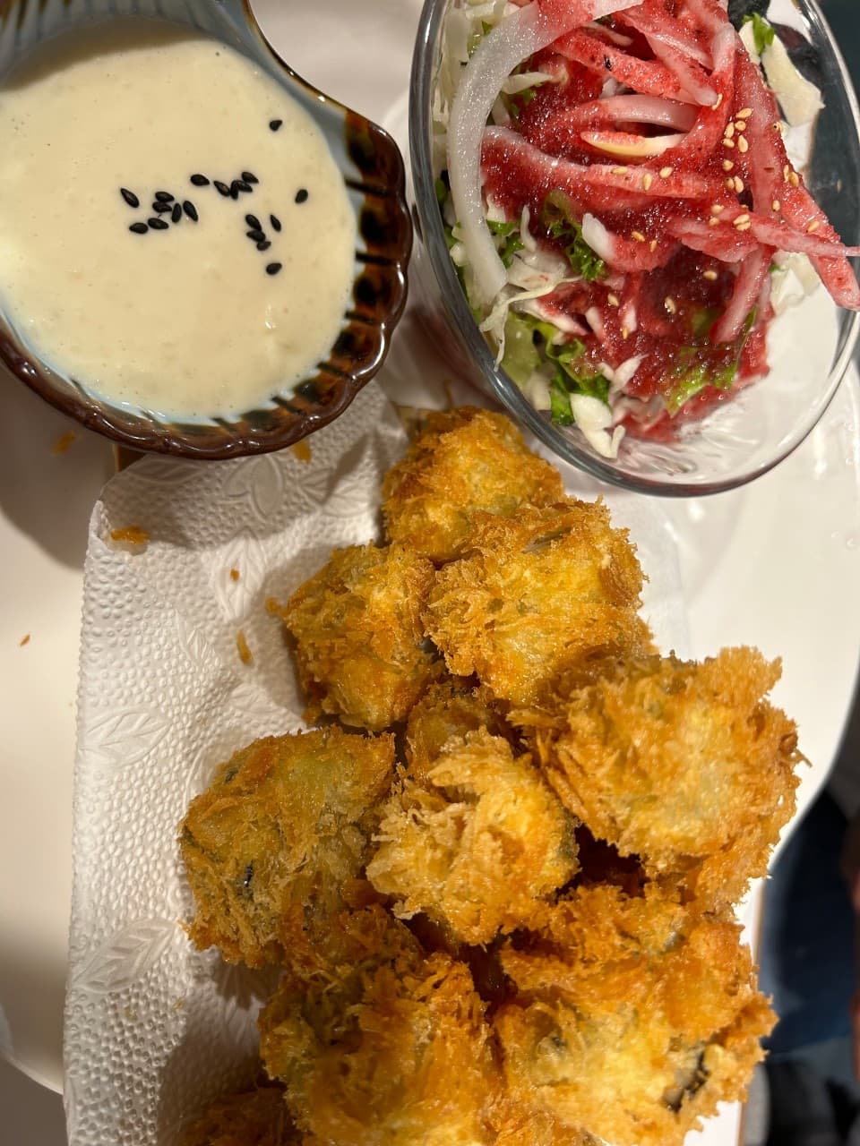 경상북도 포항시 텐구 본점 포항 이자카야 다찌석 1인 상차림. 조명 아래 바삭한 튀김과 검은 깨가 뿌려진 소스 및 샐러드가 차려진 혼술 상황.