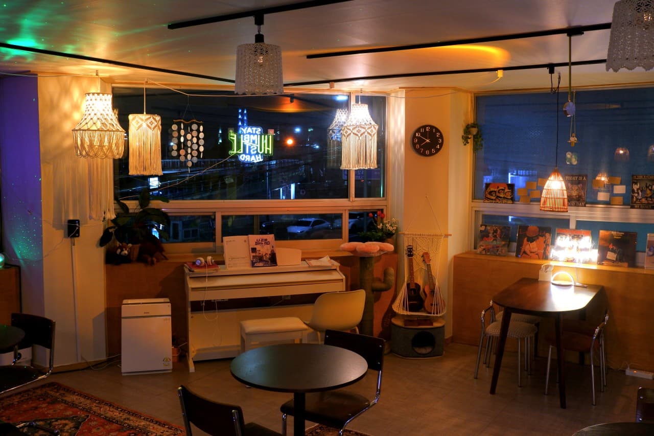 경상북도 포항시 맥주 호프 낮잠 - 오렌지색 펜던트 조명과 피아노, 원형 테이블이 놓인 실내. 창가 1인 좌석과 LP판이 진열된 혼술 공간 구성.