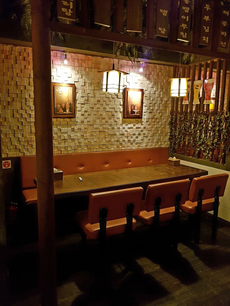 경상북도 포항시 동마실행랑채 포항 맥주 호프 - 노란 조명 아래 나무 테이블과 갈색 의자가 배치된 1인 혼술 공간. 벽돌 무늬 벽면과 상단에 걸린 메뉴판이 조화를 이룸.