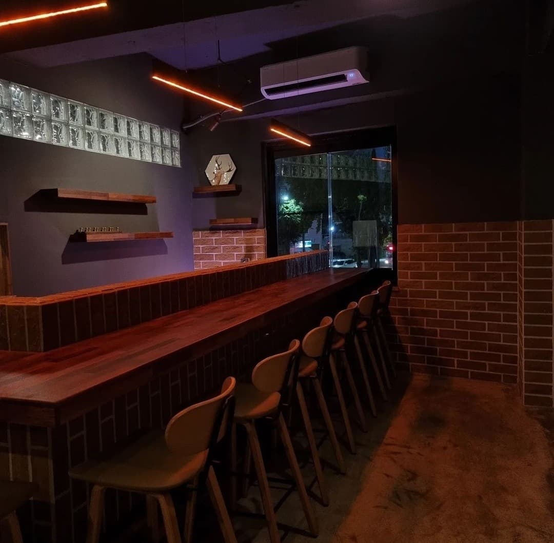 경상북도 포항시 요리주점 사슴 포항 - 주황색 선형 조명이 비추는 나무 질감 다찌석과 1인 좌석, 벽돌 인테리어가 어우러져 혼술을 즐기는 상황