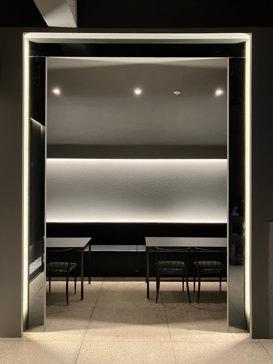 대구광역시 중구 이자카야 키르아 대구의 직선형 간접 조명 아래 배치된 블랙 테이블과 1인 좌석. 어두운 무채색 벽면과 타일 바닥으로 구성된 내부.