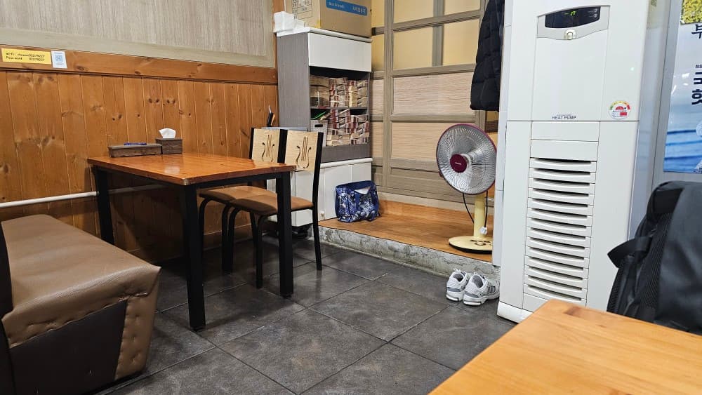 부산광역시 연제구 초원통닭 부산시청 치킨 닭강정 - 목재 벽면과 사각 테이블이 배치된 매장 내부. 혼술이나 혼밥을 위해 마련된 좌석과 실내 온열기가 놓인 전경